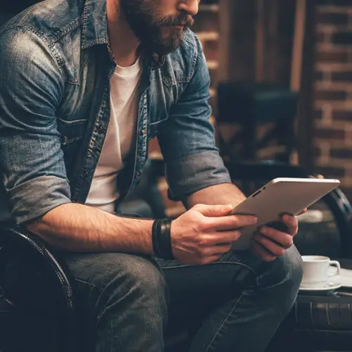 Man relaxing in masculine lounge space with tablet and coffee—The Apex Lounge client reviews section