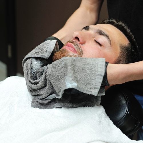 Man receiving hot towel grooming treatment as part of FlashGroom service with red light therapy